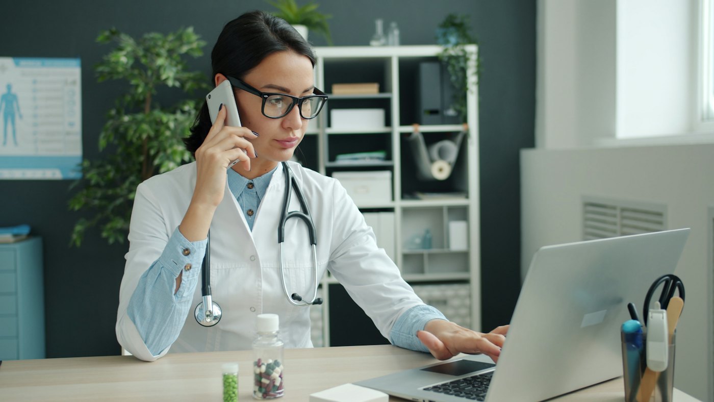 Médica ao telefone trabalhando no computador